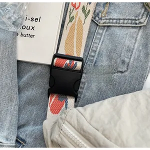 Detail view of floral print woven strap and black plastic buckle on off-white canvas bag