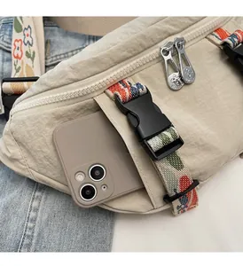 Detail of beige nylon chest bag with colorful floral strap showing phone pocket storage