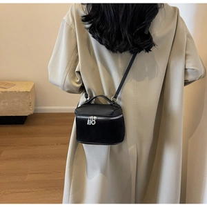 Close-up of a black lychee leather box bag worn with a beige trench coat for style