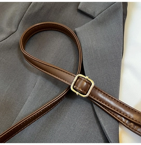 Detailed macro view of the brown synthetic leather strap with a gold square metal buckle