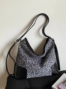Leopard print canvas tote bag with black leather straps leaning against a white wall