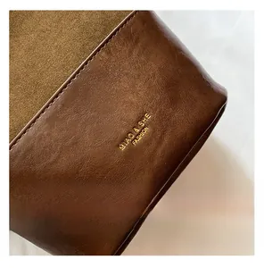 Detailed close-up of dark brown lychee leather texture and golden logo on crossbody bag