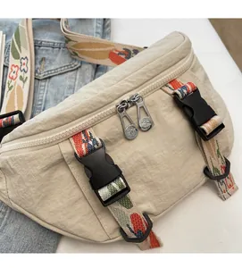 Close-up of beige canvas chest bag with double zippers and colorful embroidered strap