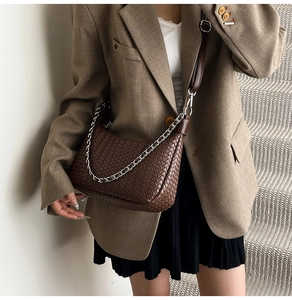 Détail d'un sac demi-lune tressé marron avec une chaîne argentée et bandoulière en cuir