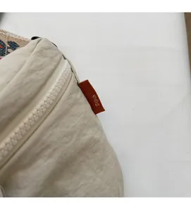 Detail of beige nylon chest bag showing thick plastic zipper and red brand side label
