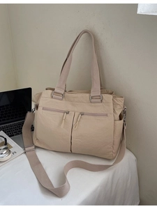 Large beige nylon tote bag with multiple pockets and adjustable strap on a minimalist desk