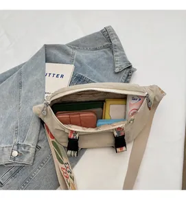 Detail view of the spacious inner compartment and floral strap of the beige canvas sling bag