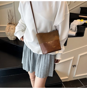 Detail of two-tone brown bucket bag featuring suede and smooth leather on a model