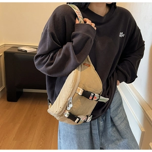 Detail view of khaki canvas chest bag with decorative woven strap and metal zippers