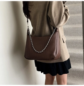 Detail of dark coffee woven leather texture with silver chain on a stylish shoulder bag