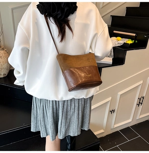 Close-up of two-tone brown suede and leather bucket bag worn by a model in an indoor setting