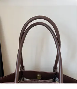 Close-up of durable brown leather dual handles and magnetic closure on tote bag