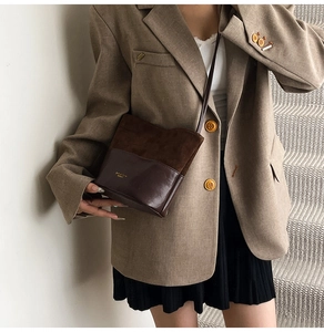 Detail of a brown patchwork crossbody bag with suede finish and gold metal logo