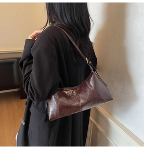 Détail d'un sac baguette en cuir verni brillant marron foncé avec une texture vintage