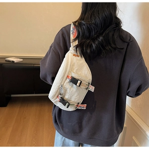 Detail of cream white canvas chest bag featuring patterned webbing strap and buckle on model
