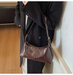 Vue détaillée du sac à bandoulière en cuir marron foncé brillant porté avec un blazer noir