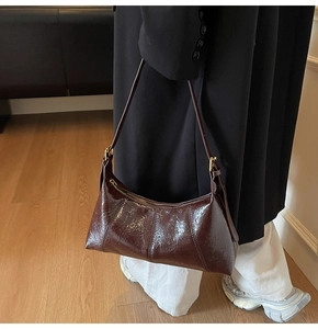 Détail du sac dumpling en cuir verni marron foncé avec texture plissée brillante et sangle
