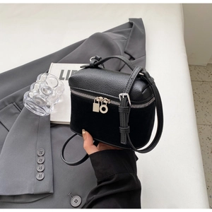 Detail of black mini box bag with textured leather and suede stitching on minimalist background