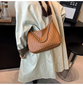 Detailed close-up of woven caramel leather hobo bag featuring a bold silver chain strap
