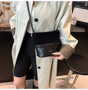 Detail of the black patchwork bucket bag with suede texture and gold logo on beige coat