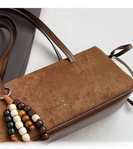 Detail of brown faux suede shoulder bag with embossed text and beaded tassel pendant
