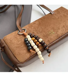 Detail of suede underarm bag featuring colorful wooden beads and metallic logo accents