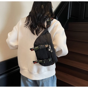 Detail of black nylon chest bag with colorful woven strap and metal zippers in sporty style