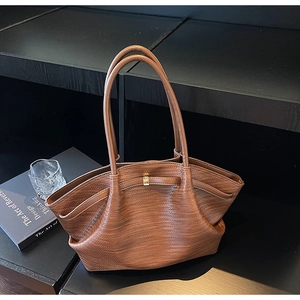 Close-up of brown woven texture PU tote bag with elegant gold buckle on a black display