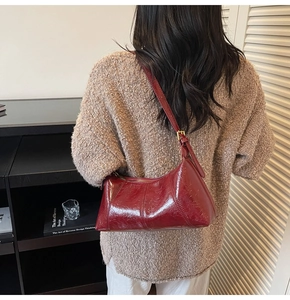 Dark red glossy leather baguette bag worn over the shoulder with adjustable strap