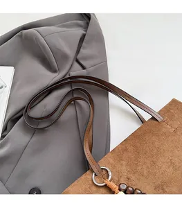 Close-up of brown suede tote bag featuring comfortable leather straps and wooden bead tassel