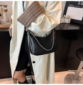 Detail of high-quality woven black leather shoulder bag with silver chain strap on model