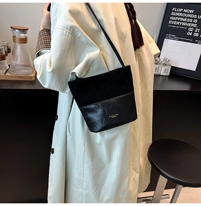 Detail of minimalist black patchwork bucket bag with golden brand logo and thin strap