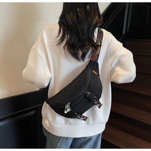Detail of black nylon chest bag featuring colorful embroidered wide strap and metal zippers