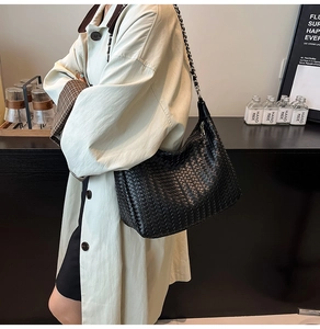 Detail shot of black woven hobo shoulder bag with metal chain strap worn by a model