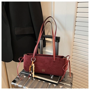 Detail of burgundy suede shoulder bag with golden lettering and beaded tassel charm