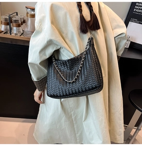 Close-up of black woven leather shoulder bag with silver chain in a cafe setting