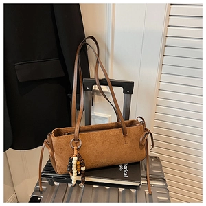 Detailed texture of brown suede tote bag featuring a beaded pendant on a silver suitcase