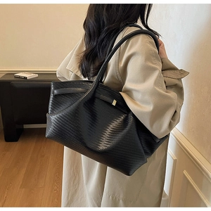Detail of black woven leather tote bag showing texture and shoulder strap on model
