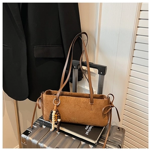 Brown suede tote bag on suitcase with beaded charm and minimalist business casual styling