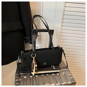 Detail of black suede shoulder bag with golden logo and decorative wood bead charm