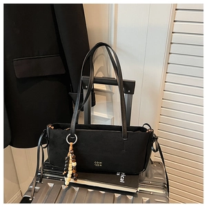Detail of black suede tote bag with wooden bead charm on a silver suitcase