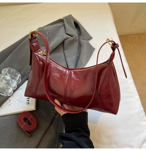 Detail of dark red patent leather handbag with adjustable strap and gold hardware