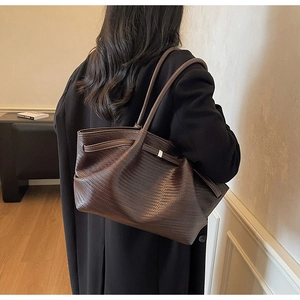 Detail of dark brown tote bag with woven texture showing the shoulder strap and soft leather