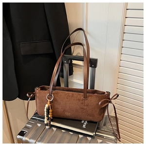 Detail of dark brown faux suede shoulder bag with ribbon bows and beaded charm on suitcase