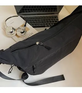 Dettaglio borsa a tracolla in nylon nero con cerniere argentate su una scrivania