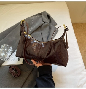 Detail of dark brown patent leather baguette bag featuring vintage wrinkled texture and gold hardware