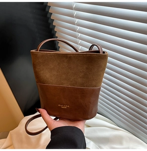Detail view of brown patchwork bucket bag featuring suede texture and gold logo text