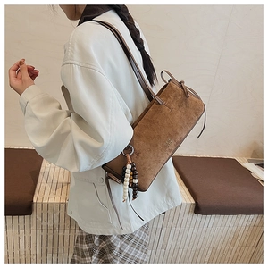 Detail of dark brown suede shoulder bag with decorative beaded tassel and gold lettering