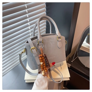 Detailed view of light gray faux leather handbag with wooden bead charm and gold hardware