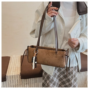 Detail of brown suede tote bag with stylish bead charm shown in a lifestyle street setting